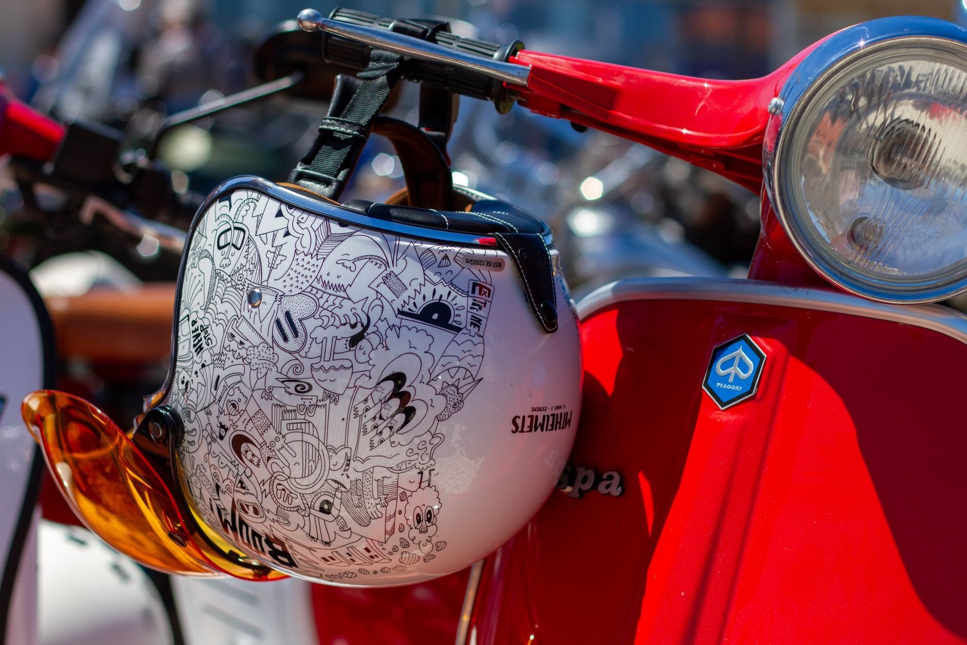 Artistic helmet hanging on a classic red scooter in bright sunlight.