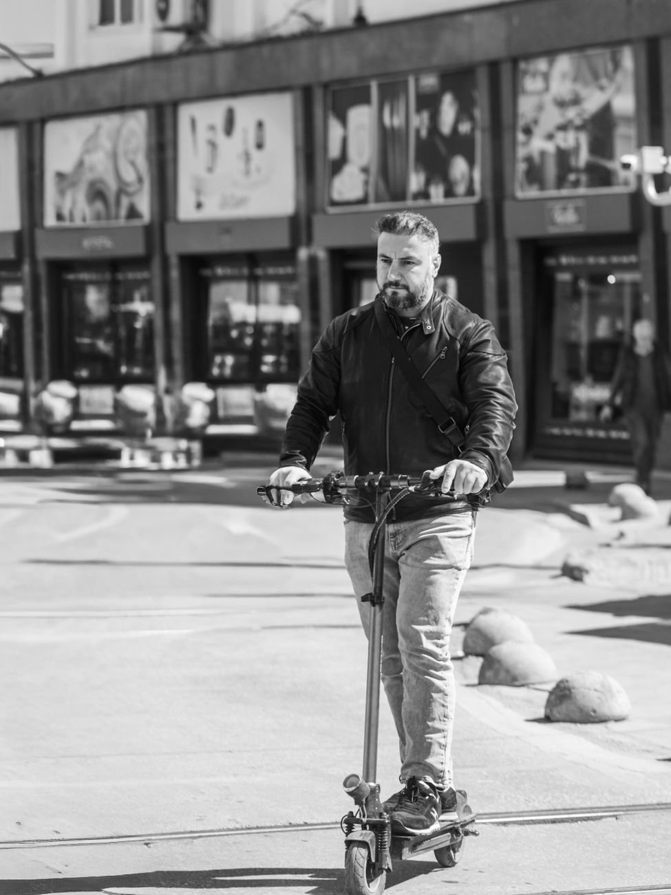 A man in casual attire riding an electric scooter on a city street in black and white.
